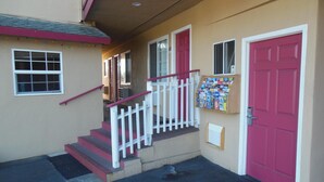 A building entrance with a red door, a small set of stairs, and a book display outside. - Sealamp Inn (Seaside)