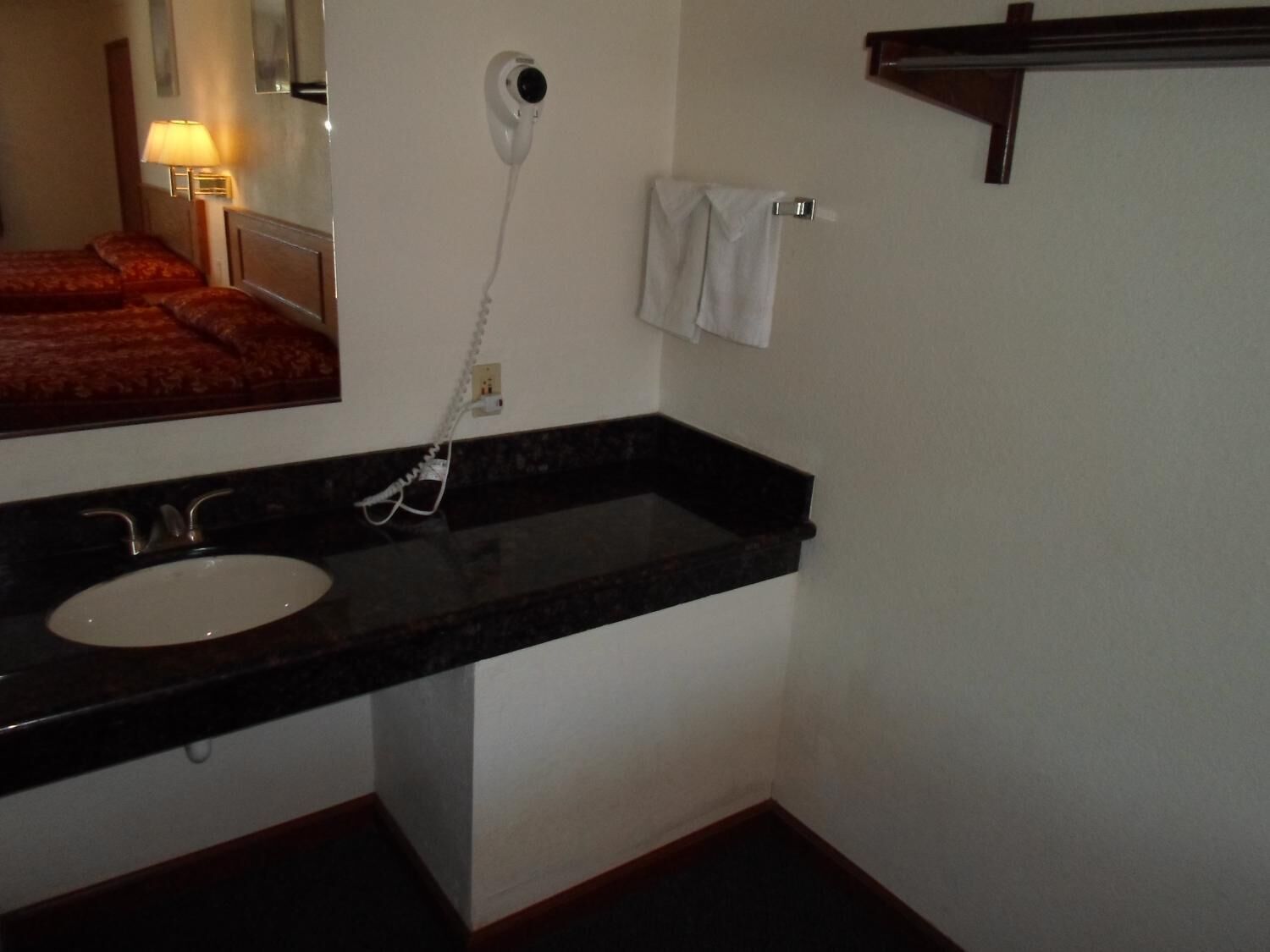 A hotel bathroom with a black countertop sink, a mirror, a hairdryer, and a towel rack.