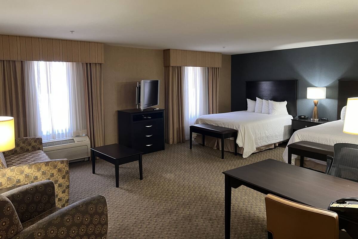 A hotel room with two beds, a desk, a chair, a dresser, a TV, and a lamp.