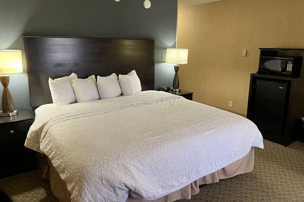 A hotel room with a large bed, two bedside tables, a nightstand, a lamp, a microwave, and a small refrigerator.