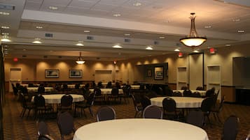 A conference room with multiple tables and chairs, ceiling lights, and framed pictures on the walls.
