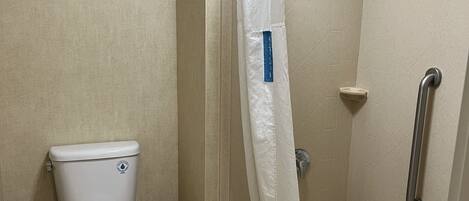 Une salle de bain équipée de toilettes, d’une douche avec une barre d’appui et d’une poubelle.