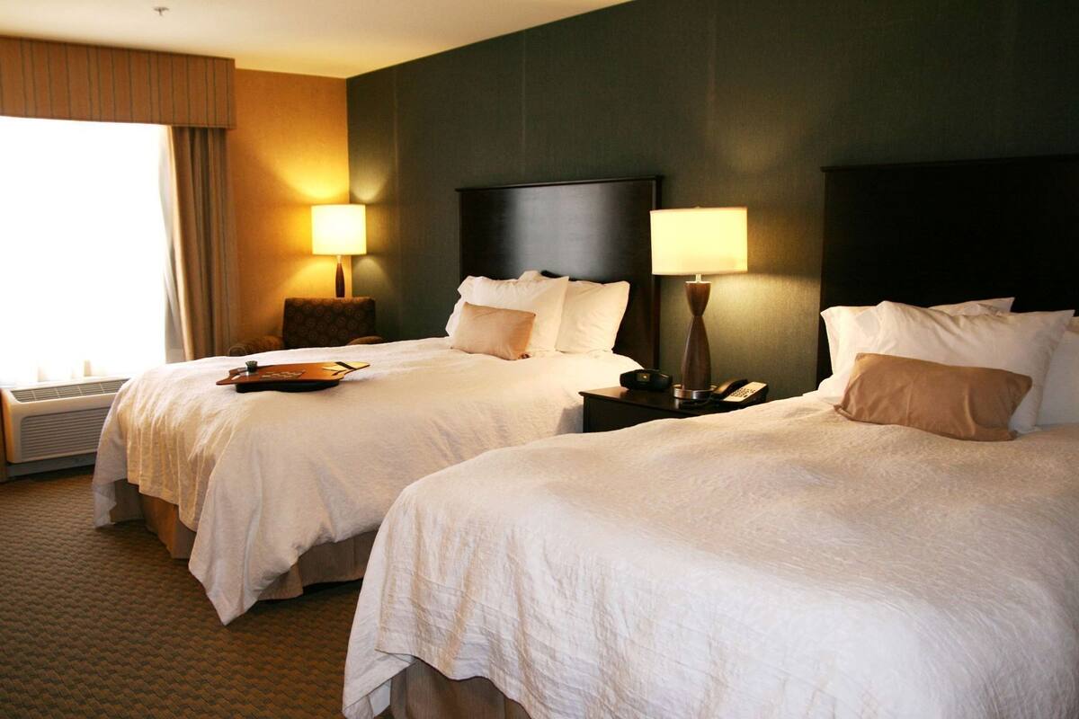 Habitación de hotel con dos camas, cada una con mesita de noche, lámpara y bandeja.
