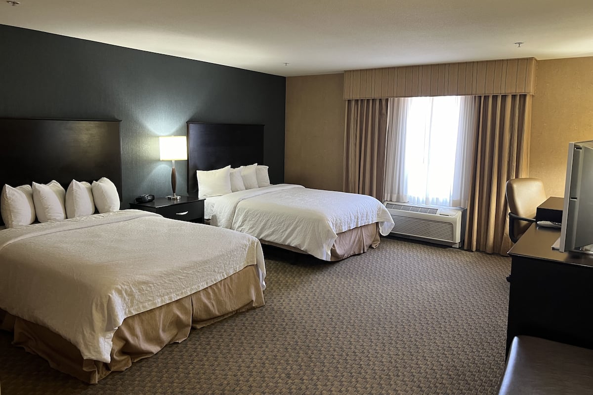 A hotel room with two beds, a desk with a computer, a lamp, and a window with curtains.
