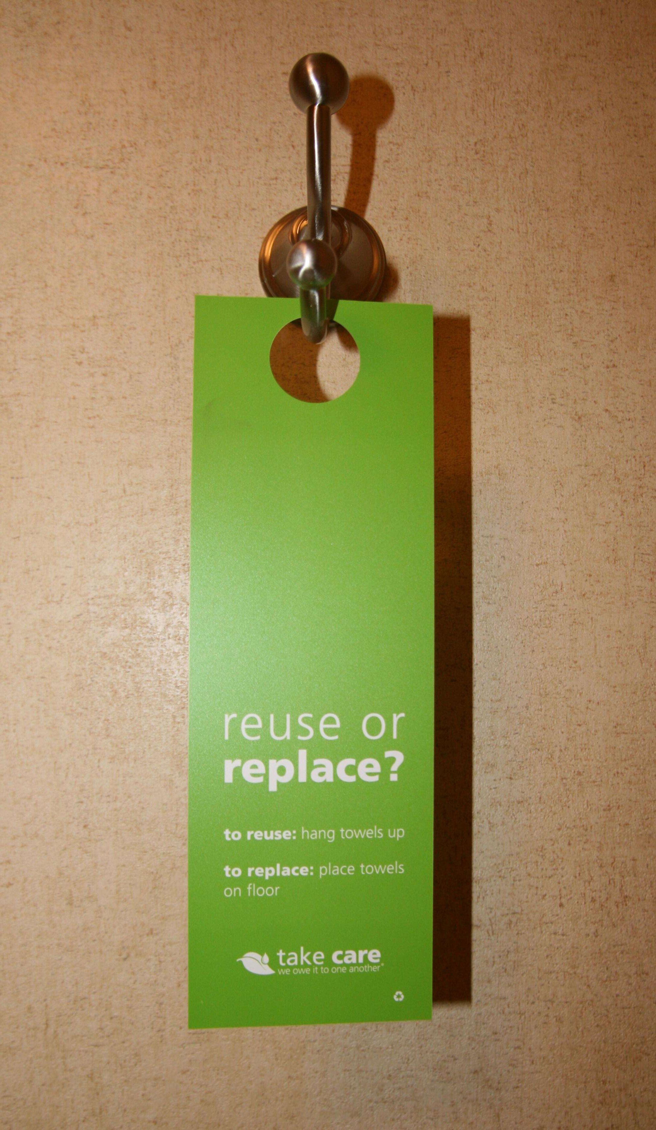 A green tag with instructions on towel reuse or replacement, hanging from a door handle.