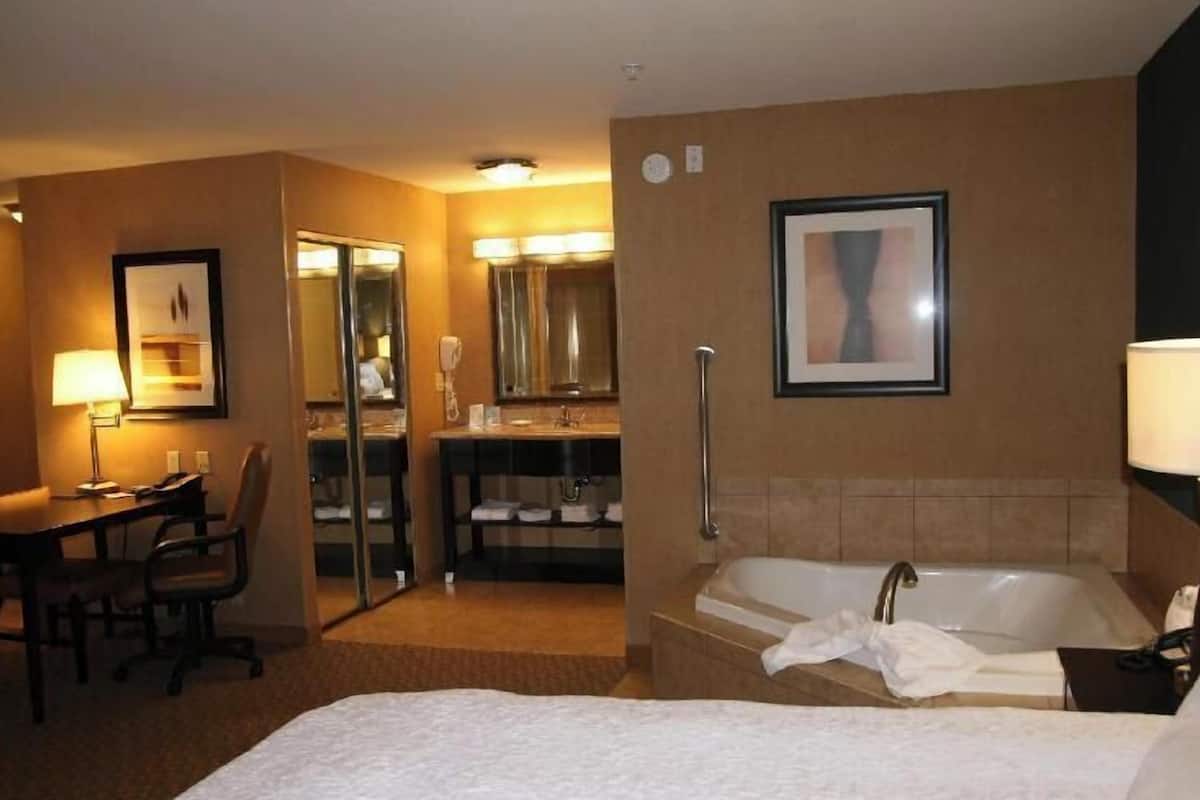A hotel room with a bed, a desk, a chair, a bathroom with a bathtub, and a mirror.