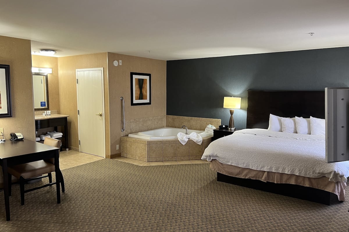 A hotel room with a bed, a desk, a chair, a bathroom with a bathtub, and a mirror.