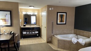 Un baño de hotel con una bañera grande, un tocador con espejo y un escritorio con una silla.