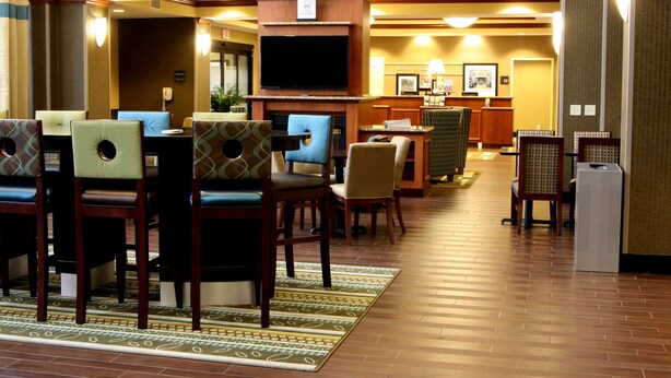 Et hotellobby med receptionsdisk, fjernsyn og flere siddeområder med stole og borde.