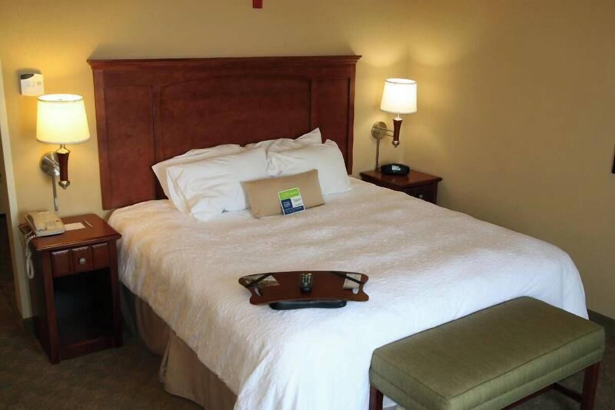 Habitación de hotel con una cama grande, dos mesitas de noche, una lámpara de noche, una bandeja con bebida y un banco verde.