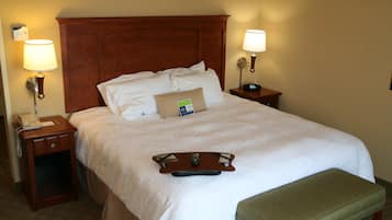 Une chambre d’hôtel avec un grand lit, deux tables de chevet, une petite table, un banc vert et un plateau avec une télécommande.