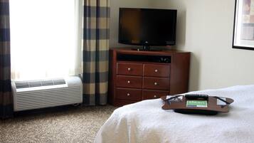 Habitación de hotel con cama, televisor sobre un mueble de madera, control remoto y un cartel que indica 'limpio' en la cama.