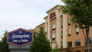 Et Hampton Inn & Suites skilt med et klassisk design, en stor bygning med mange vinduer og et amerikansk flag.