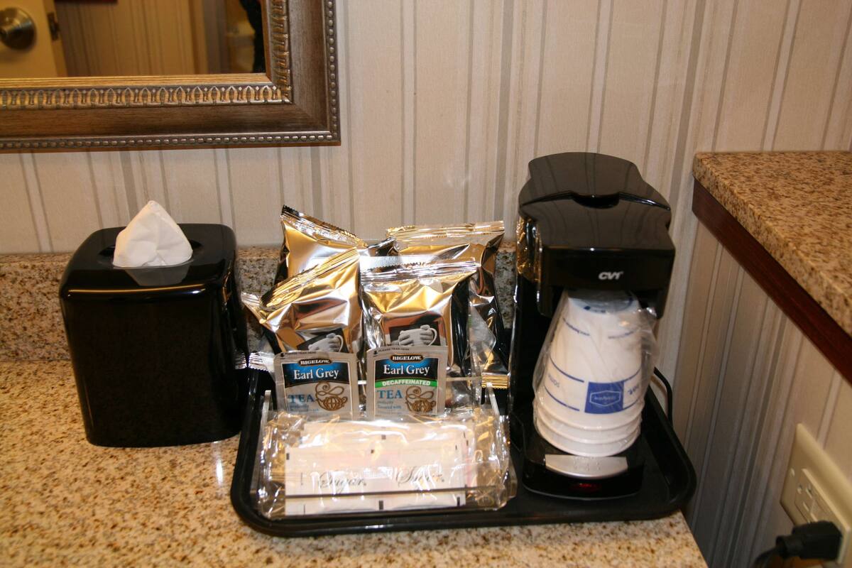 Una estación de café con cafetera, bolsitas de té y dispensador de agua sobre una encimera de granito.