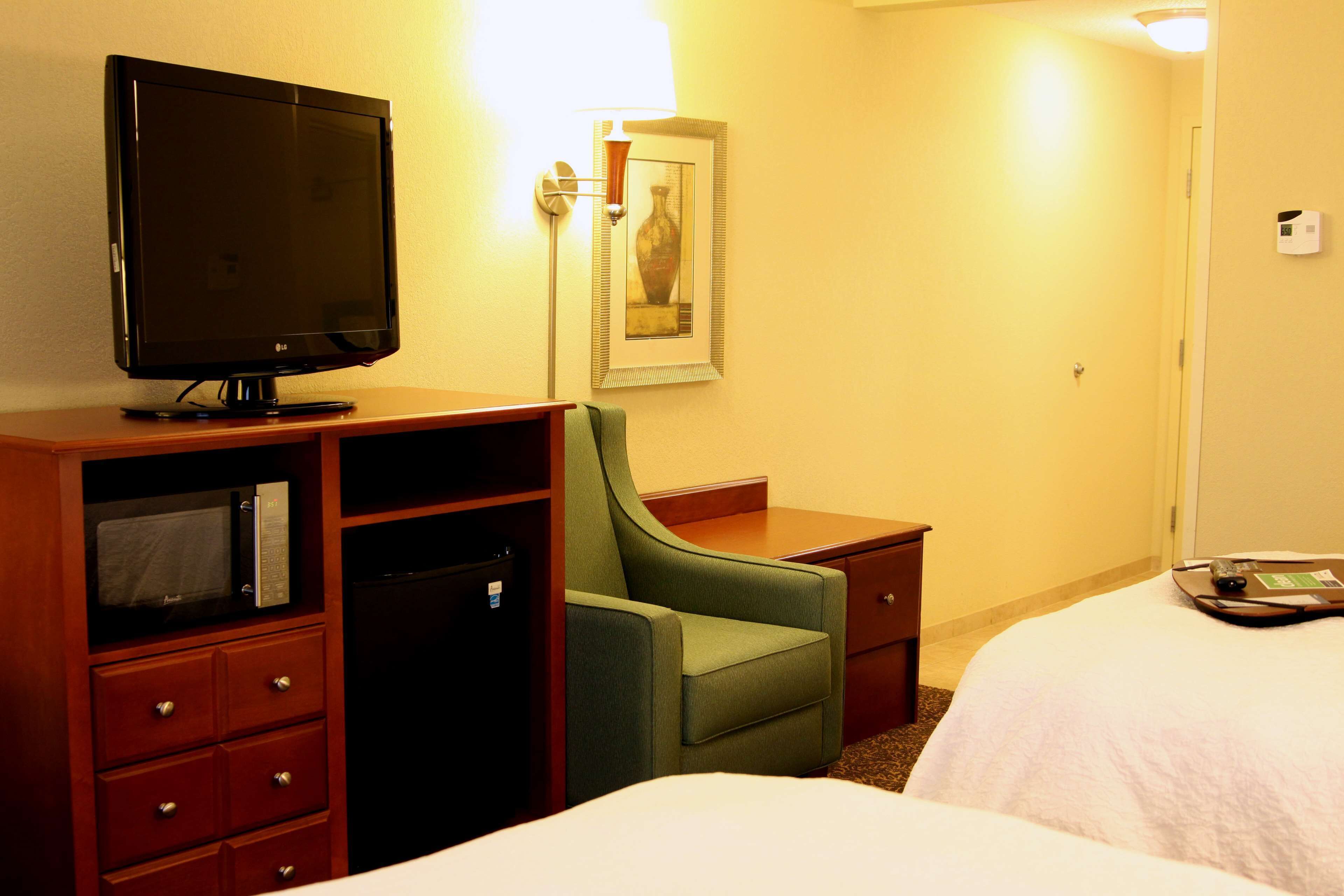 Quarto de hotel com televisão, escrivaninha, uma cadeira e duas camas.