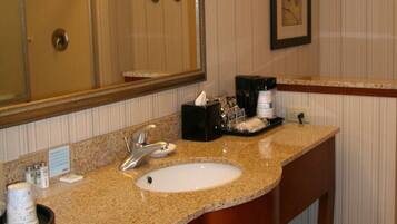 A hotel bathroom with a granite countertop sink, a large mirror, a towel rack, and a framed picture on the wall.