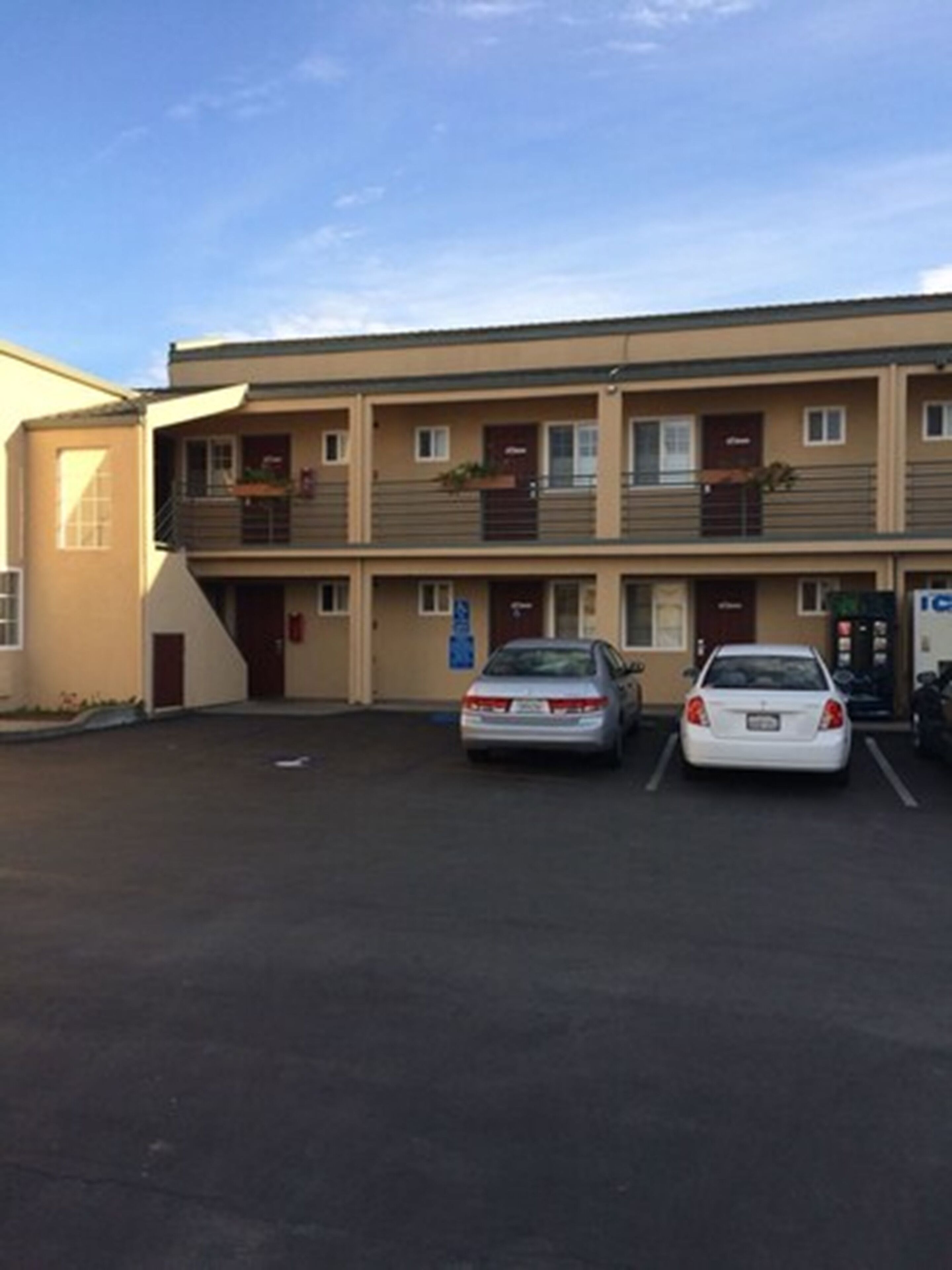 A motel with a parking lot, two cars parked, and a signboard.