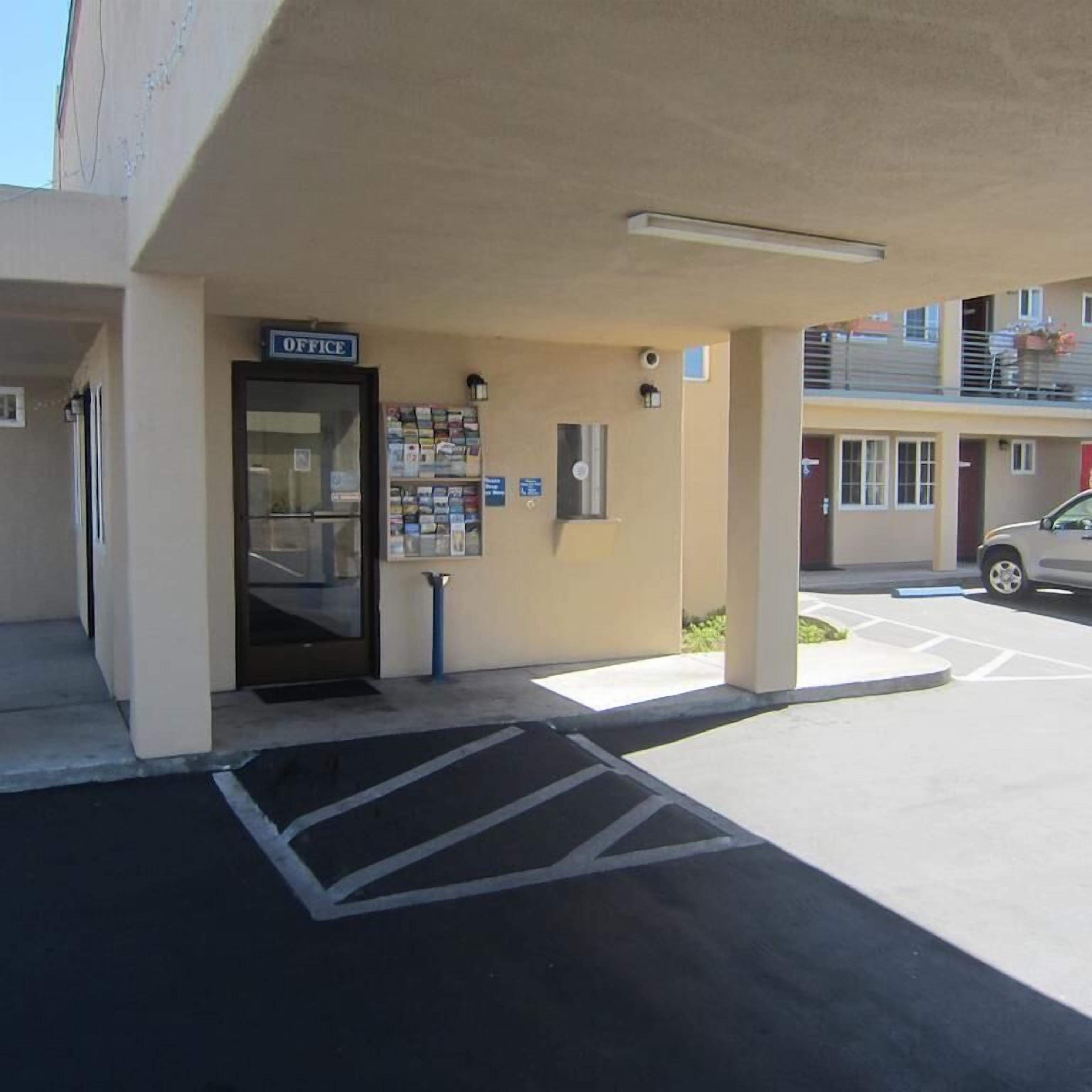 Een gebouw met een 'OFFICE' bord, een parkeerplaats met aangewezen parkeerplaatsen voor mindervaliden, en een auto op de parkeerplaats.