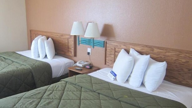 A hotel room with two beds, each with green quilts and white pillows. There is a nightstand with a lamp and a telephone. - Pacific Best Inn (Seaside)