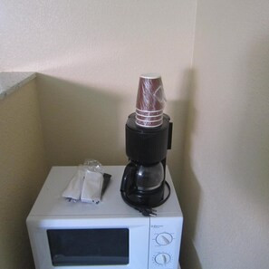 A microwave with a coffee maker on top, a tissue box, and a plastic bag.