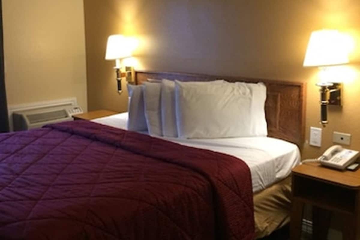 A hotel room with a bed, two bedside lamps, a telephone, and a heater.