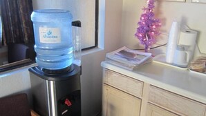 A water dispenser, a small decorative tree, a coffee maker, and a trash bin in a hotel room. - Pacific Best Inn (Seaside)