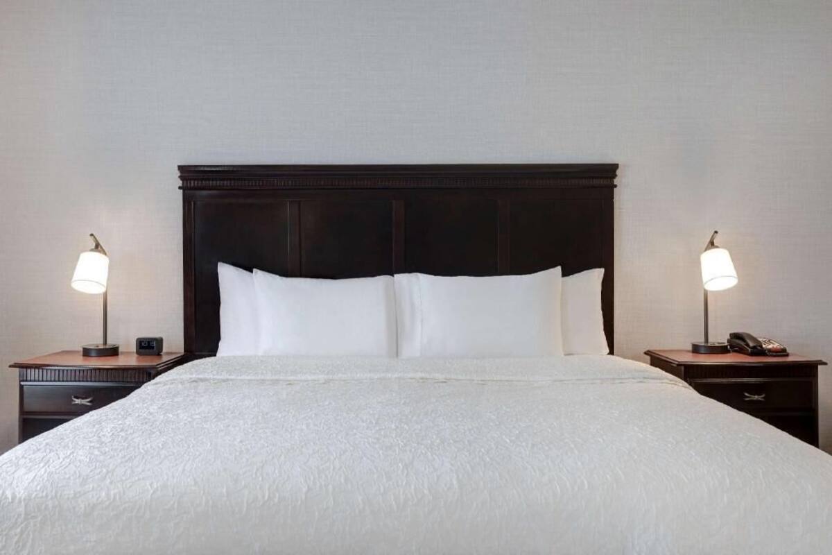 A hotel room with a large bed, two bedside tables with lamps, a clock, and a phone on one of the tables.