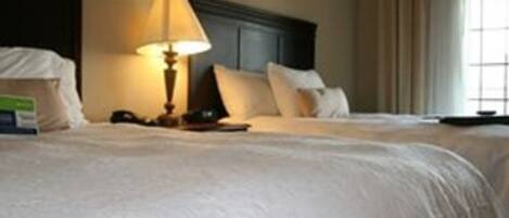 Una habitación de hotel con una cama grande, una lámpara de noche y un ventanal con cortinas.