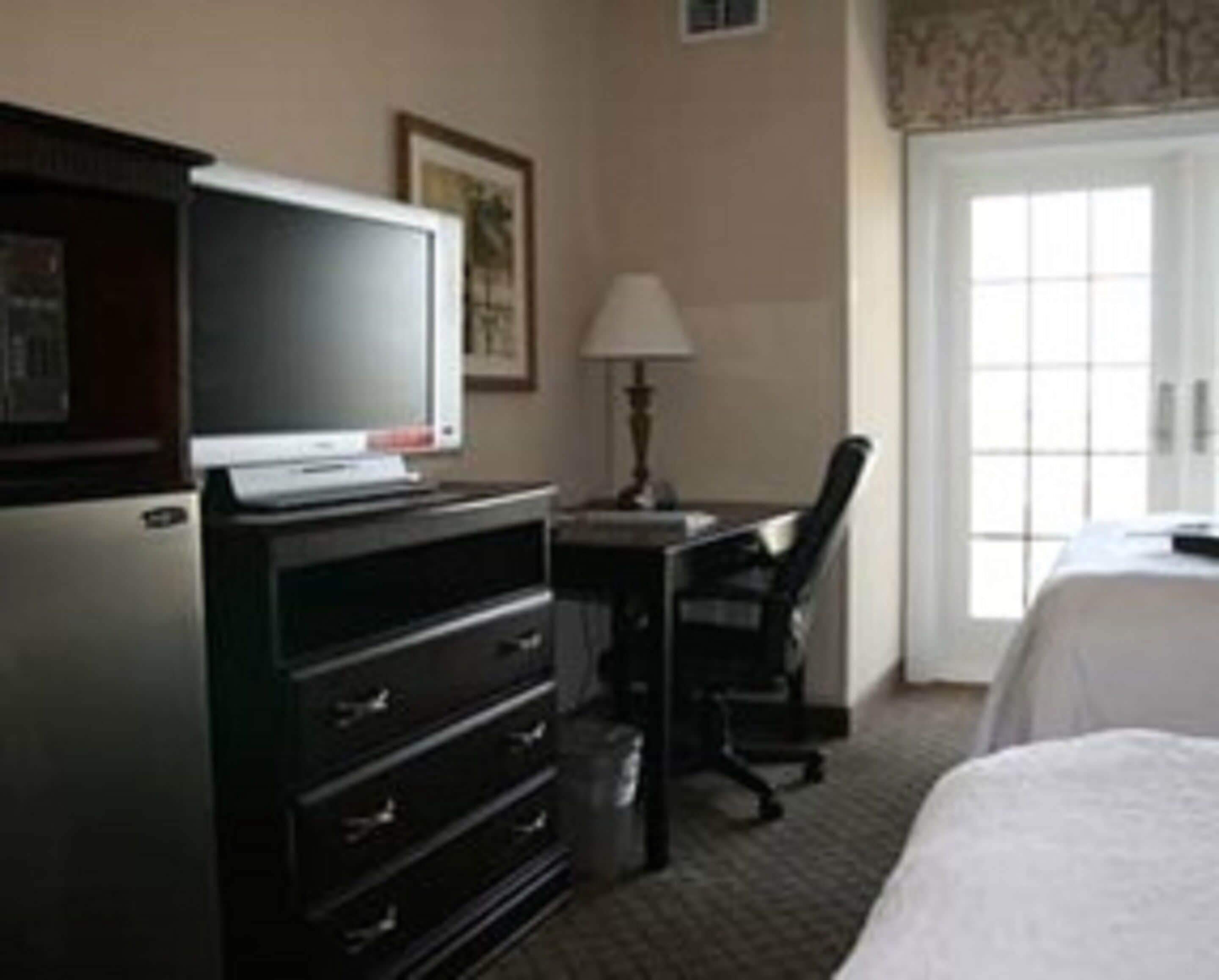 A hotel room with a bed, a desk, a chair, a television, and a dresser.