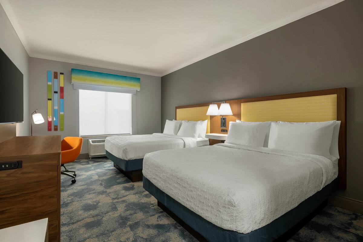 A hotel room with two beds, a desk, a chair, and a window with a view.