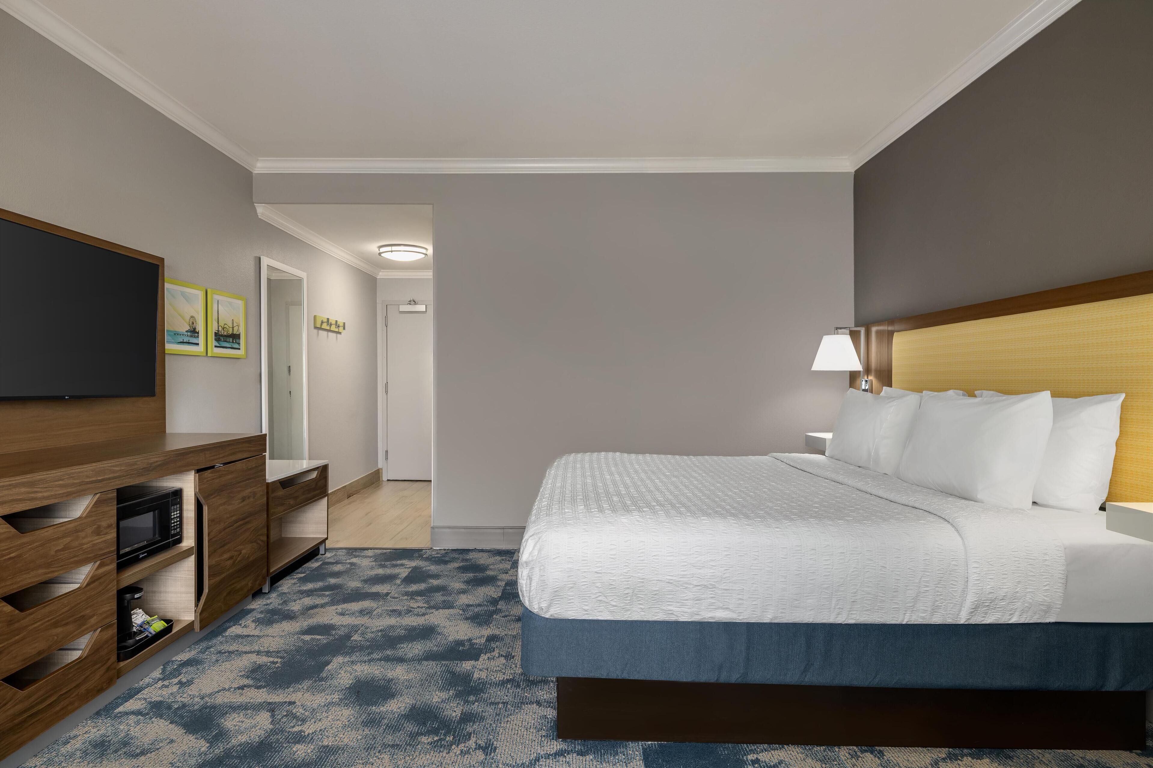 Una habitación de hotel con una cama grande, un televisor sobre un mueble de madera y un pasillo que lleva a una puerta.