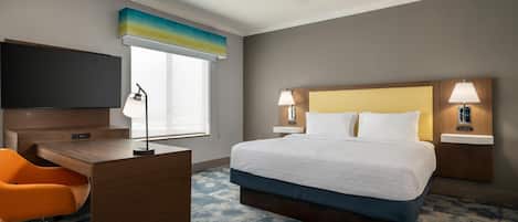 A hotel room with a bed, desk, chair, and a television.