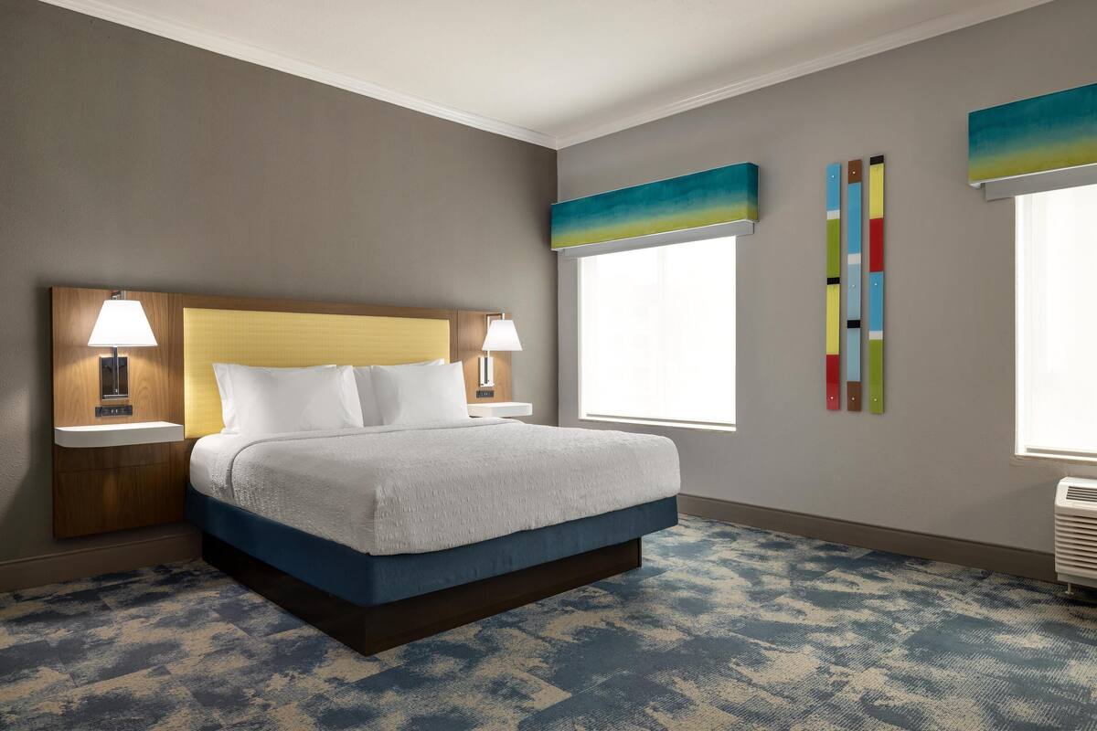 A hotel room with a bed, nightstands, a window, and wall art.