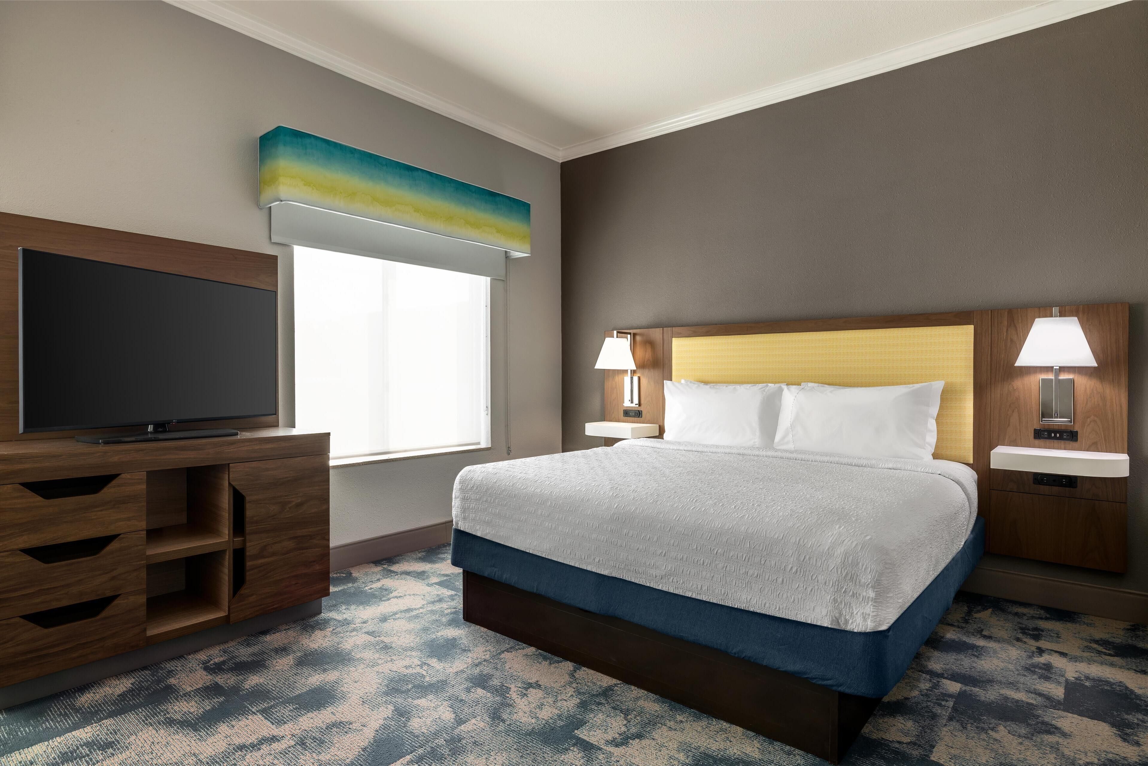 A hotel room with a bed, a TV, a desk, and a window.