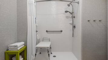 A walk-in shower with a grab bar, a wheelchair-accessible bench, and a shelf with folded towels.