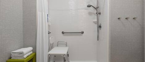 A walk-in shower with a grab bar, a wheelchair-accessible bench, and a shelf with folded towels.