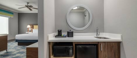 Una habitación de hotel con cama, baño con espejo, lavamanos, microondas y refrigerador.