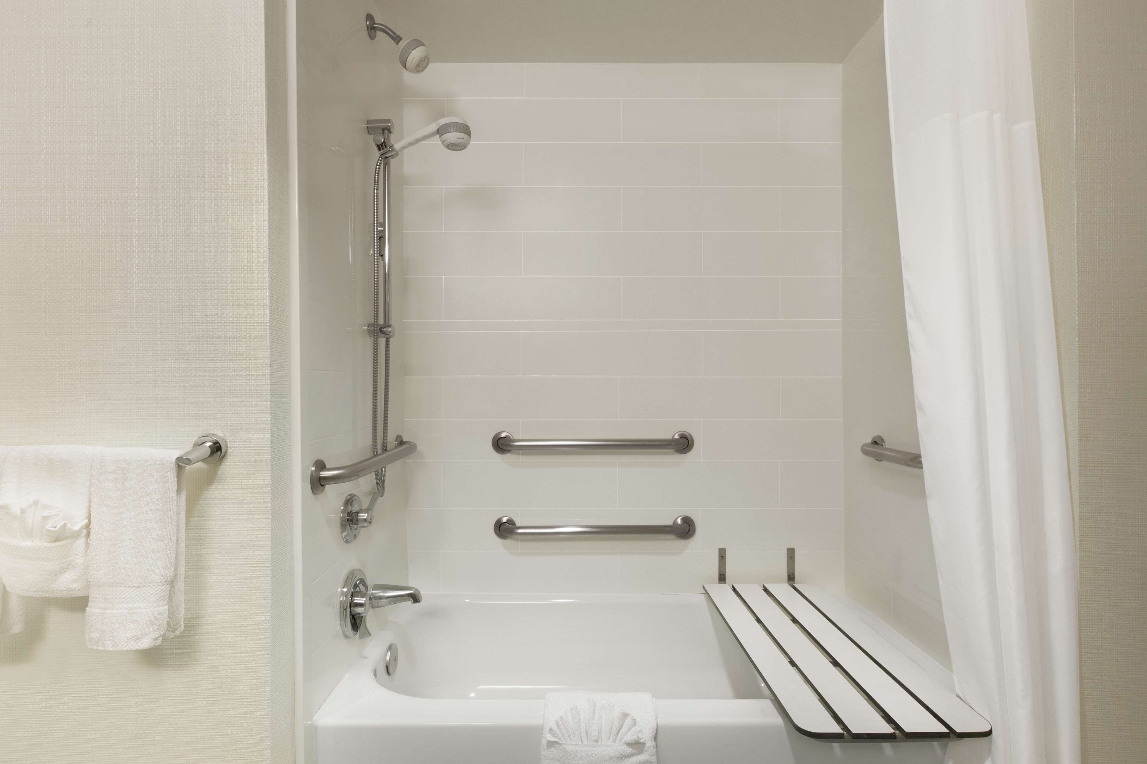 Un baño moderno con bañera, barras de apoyo y un perchero para toallas.