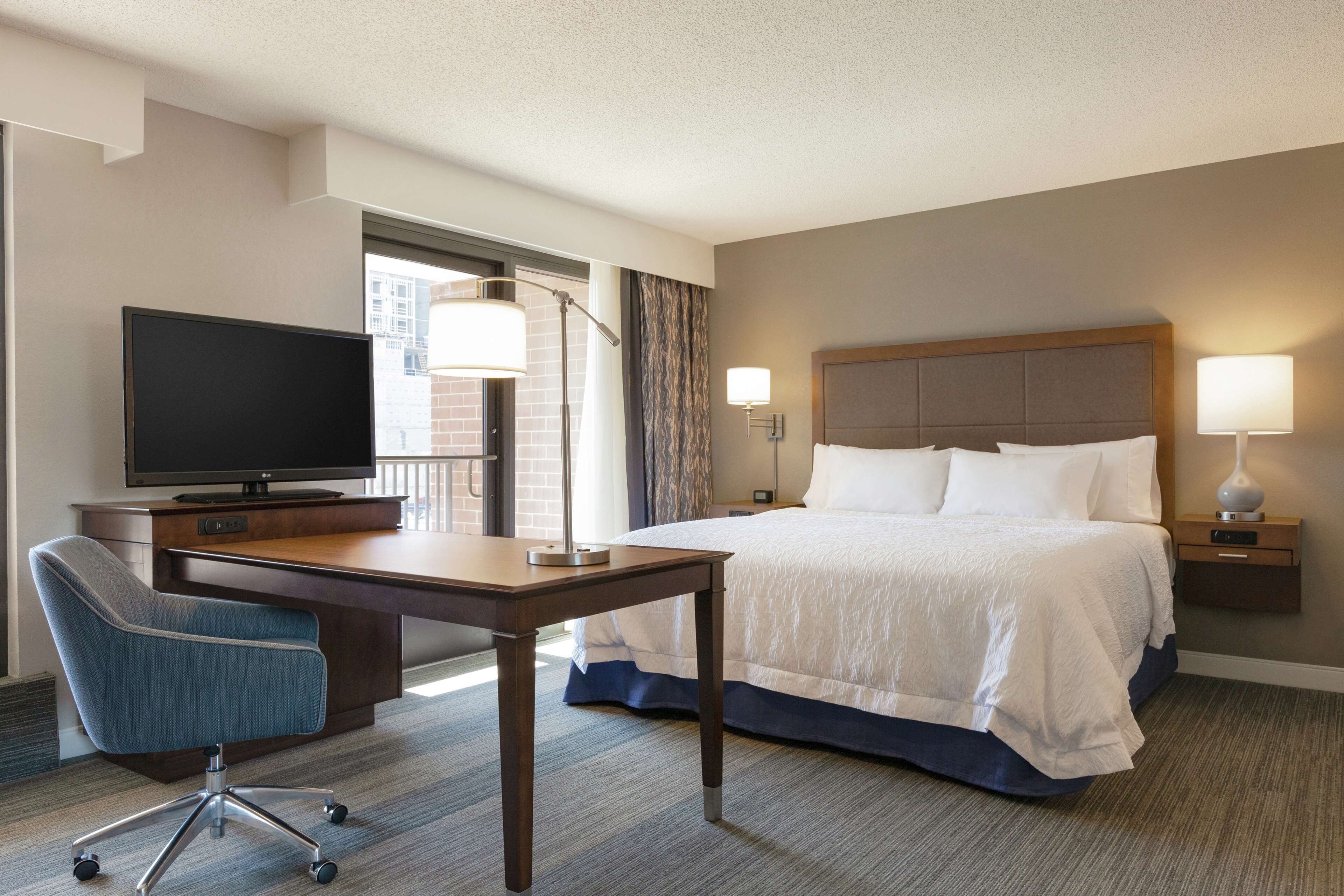 A hotel room with a bed, desk, chair, TV, and lamps.