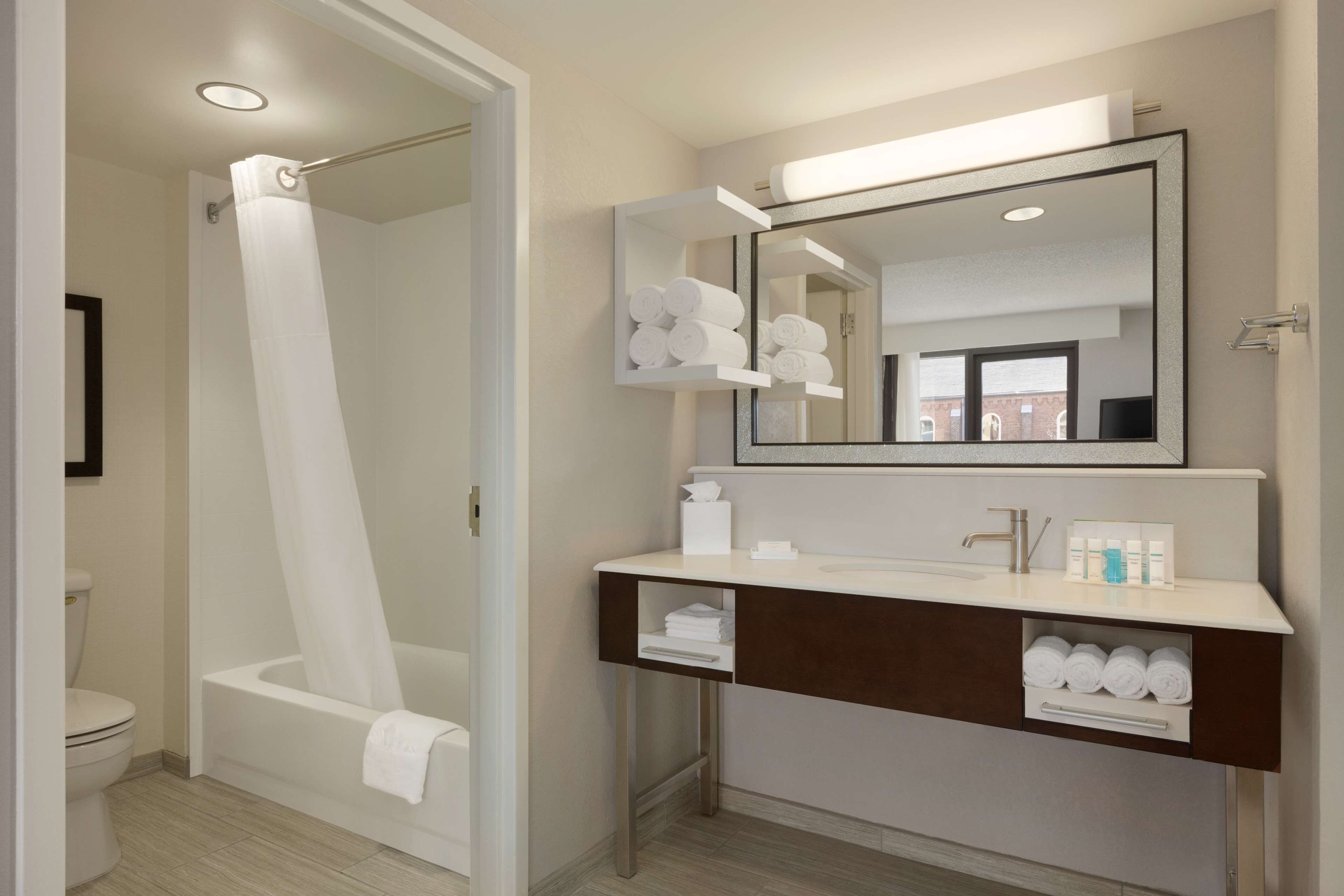 A modern bathroom with a bathtub, a vanity with a mirror, and shelves holding towels.