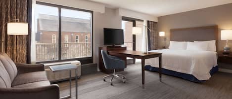 A hotel room with a bed, a desk, a chair, a television, and large windows.