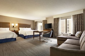 A hotel room with two beds, a desk, a TV, and a sofa.