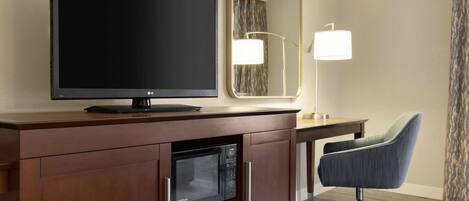 Quarto de hotel com televisão de tela plana, micro-ondas, escrivaninha com luminária e cadeira.