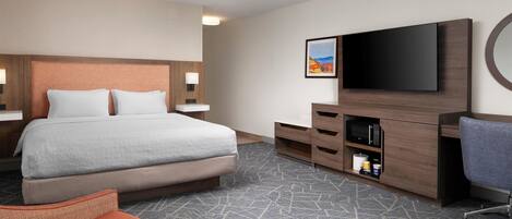 A hotel room with a bed, a TV, a desk, a chair, and a carpeted floor.