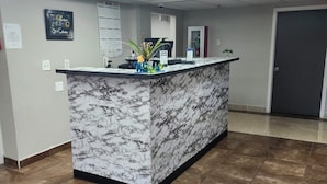 A reception area with a marble counter, a calendar, a plant, and a door.