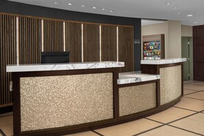 Un mostrador de recepción con encimera de mármol y paneles texturizados, una pared de listones de madera con iluminación integrada y suelo de baldosas.