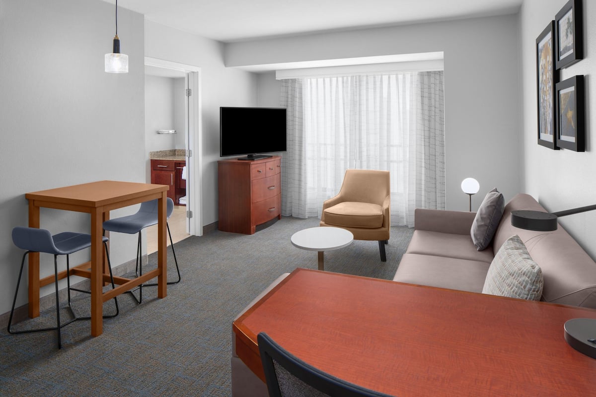 Una habitación de hotel moderna con comedor, sofá, televisor y una pequeña mesa.