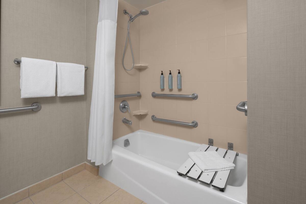 Un baño moderno con bañera, barras de apoyo, ducha y artículos de aseo.