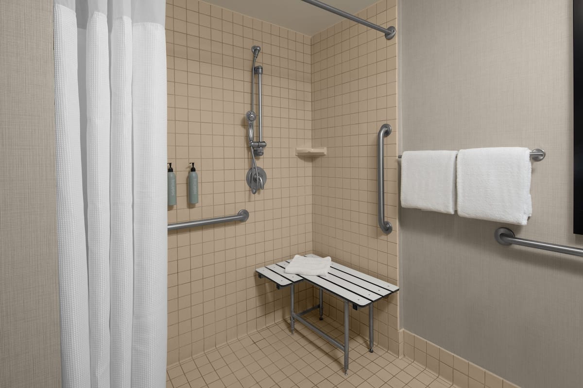 Un baño con ducha, barras de apoyo, un banco y un perchero para toallas.