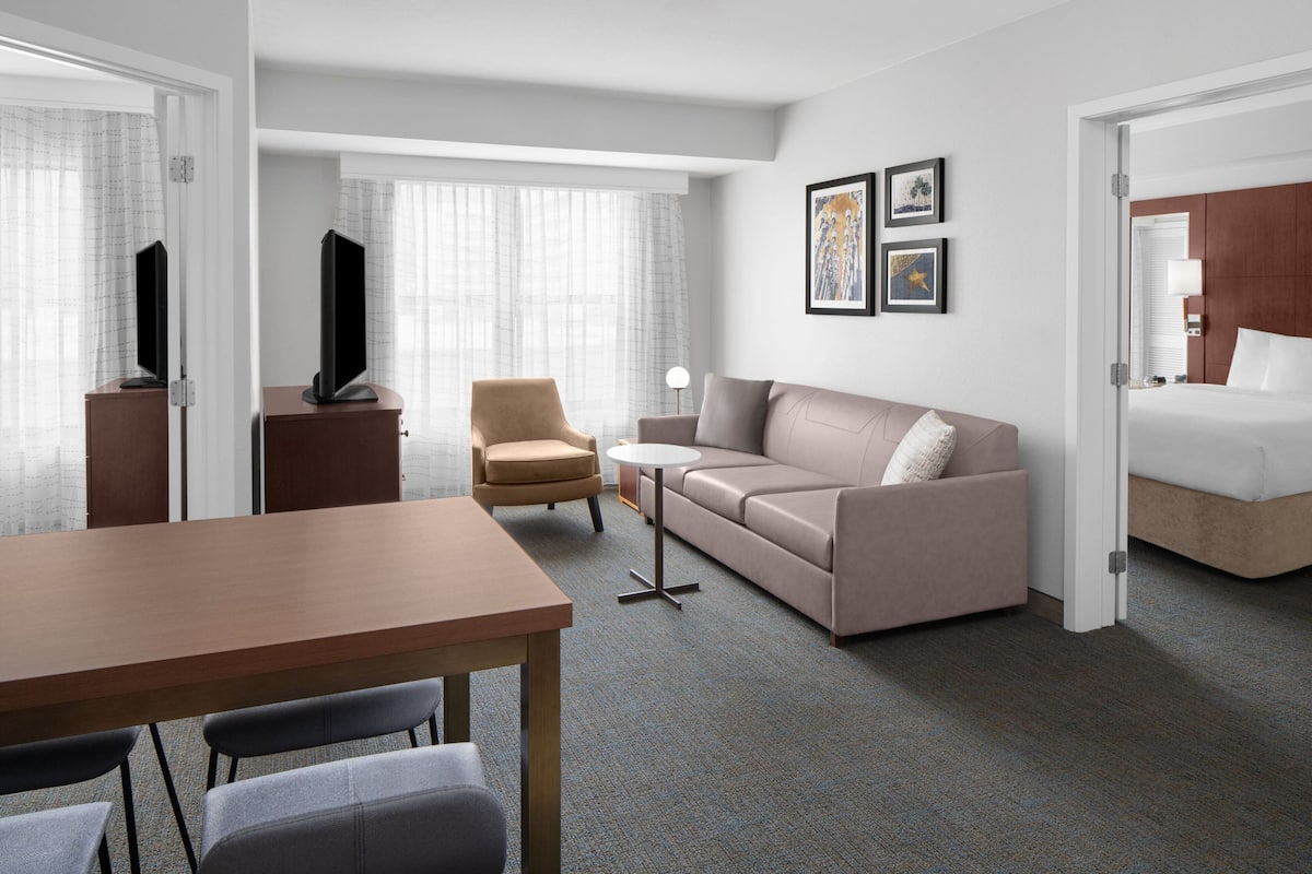 Una habitación de hotel con cama, sofá, mesa de centro, televisor y escritorio.